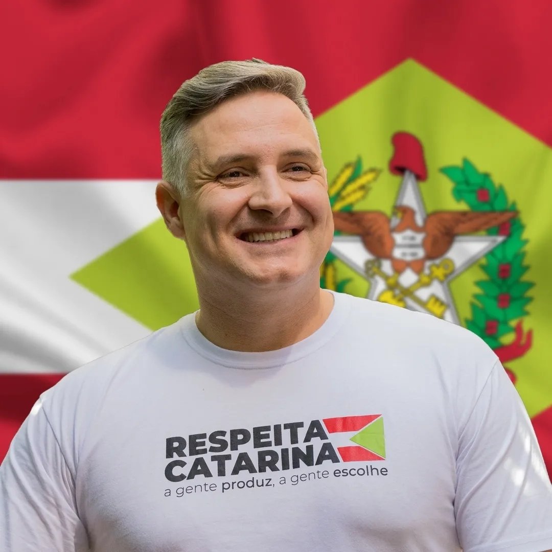 Matheus Cadorin sorrindo, diante da bandeira de Santa Catarina.
